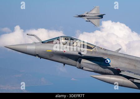 The image depicts Hellenic Air Force Dassault Rafale EG jets flying in formation while performing a banking maneuver at Athens Flying Week 2025. Twin-engine multirole fighters powered by Snecma M88-2 turbofan engines, featuring delta wings, canards, bubble cockpit canopy, air-to-air refueling probe, leading-edge root extensions, and retractable landing gear. The photograph emphasizes close-up pilot view, air-to-air display, maneuverability, supersonic performance, and operational multirole capability. Stock Photo