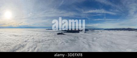 Aerial view of a landscape where islands of earth rise from a sea of clouds, sun shining above, Thann, Grand Est, France. Stock Photo