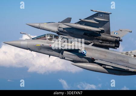 The image depicts a Hellenic Air Force Dassault Rafale EG jet performing a banking maneuver in formation during Athens Flying Week 2025. The twin-engine multirole fighter is powered by Snecma M88-2 turbofan engines and features delta wings, canards, bubble cockpit canopy, air-to-air refueling probe, and leading-edge root extensions. The photograph highlights close-up pilot view, formation flight, air-to-air demonstration, maneuverability, supersonic capability, and operational multirole performance. Stock Photo