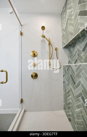 Bathroom with a gold shower head and a green tile wall. The shower head is attached to the wall and the tiles are arranged in a chevron pattern Stock Photo