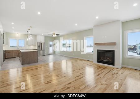 Large open living room with a fireplace and a kitchen. The room is clean and empty, with a lot of natural light coming in through the windows. The fir Stock Photo