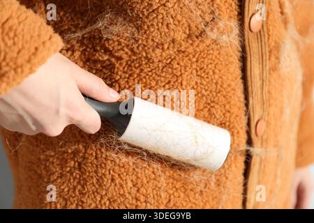 Woman cleaning cardigan with lint roller on light grey background, closeup Stock Photo