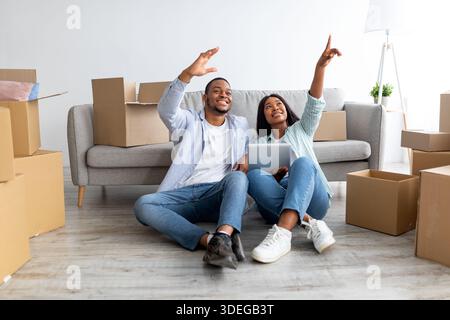 African american couple discussing design of new flat, sitting on floor and using digital tablet, planning renovation Stock Photo
