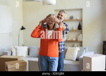 Senior couple sharing joyful moment with man surprising wife indoors Stock Photo