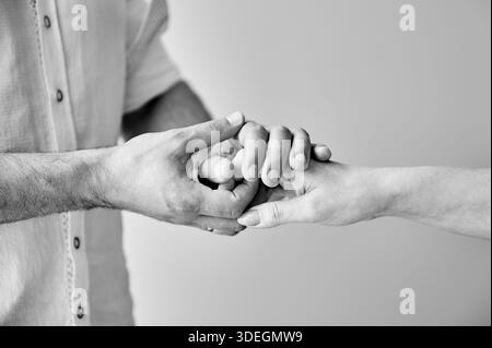 Close up of two hands engaging in delicate touch. Man's and woman's hands on white neutral background. Husband holding hand of his lovely wife. Concept of support, mutual respect. Black and white. Stock Photo