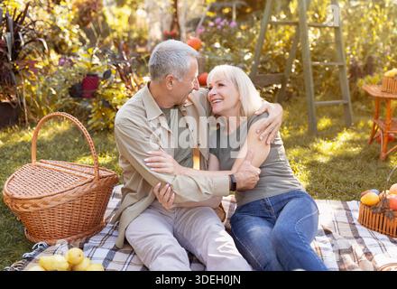 Loving senior married spouses resting in autumn park, having picnic and embracing, enjoying evening outdoors Stock Photo