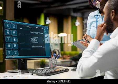 Black IT engineers team developing app and software algorithm on pc, working in the office late at night. Specialists use digital tools and focuses on script engineering and coding. Stock Photo