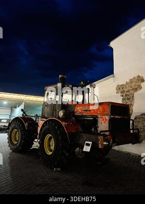 Khodakhkiv,Ukraine - November 29, 2025: Old K-700A Kirovets tractor in a courtyard at night, weathered paint, industrial farm machinery on display. Stock Photo