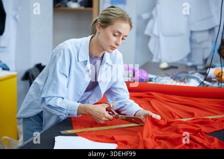 Dedicated seamstress carefully trims and assesses fabric pattern on spacious worktable Stock Photo