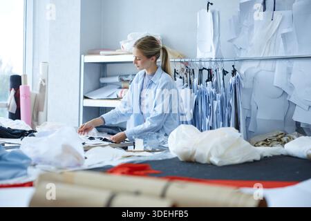 Professional clothing woman creator arranging pattern pieces meticulously during daylight in studio Stock Photo