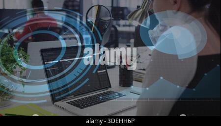 Displaying laptop screen showing code in open-plan office, developer wearing dark sleeveless top Stock Photo