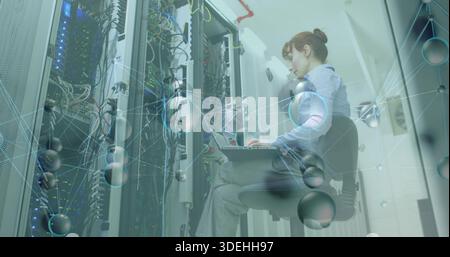 Female IT tech in shirt checking servers sitting rack aisle with laptop, patch cables, copy space Stock Photo