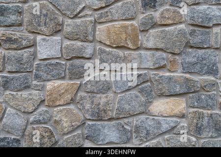 A close-up, full-frame shot of a rustic, textured natural stone wall featuring Wilmington Complex (Blue Gneiss Rocks) in Wilmington Delaware Stock Photo