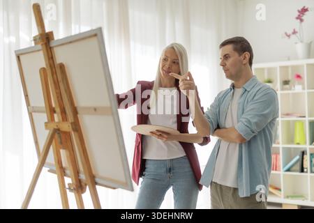 Focused artists discussing a canvas on an easel inside an art studio Stock Photo