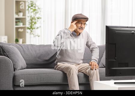 Senior man sitting on couch in front of TV and suffering from headache Stock Photo