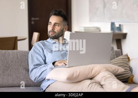 Thoughtful man working on laptop from home Stock Photo