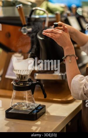 Barista preparing pour-over coffee using a manual brewing method with specialized equipment. Hot water is poured over coffee grounds in a filter. Stock Photo