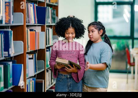 Two students standing near library shelves discussing book choice. Friendly interaction shows curiosity peer learning communication literacy growth in Stock Photo