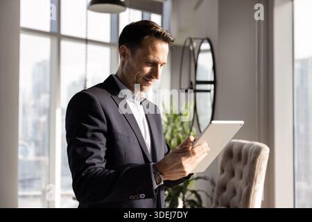 Positive young Hispanic executive man typing on tablet Stock Photo