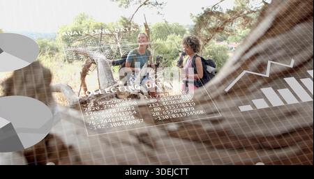 Hiking two women pausing on sunlit wooded hillside, wearing activewear with backpacks, AR overlays Stock Photo