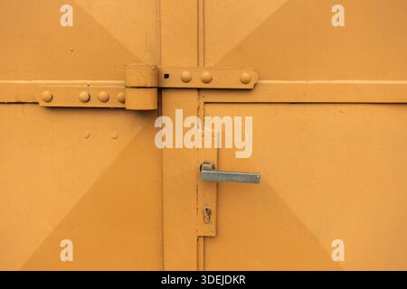 Yellow painted metal door with handle and keyhole, highlighting industrial character and textured surface Stock Photo