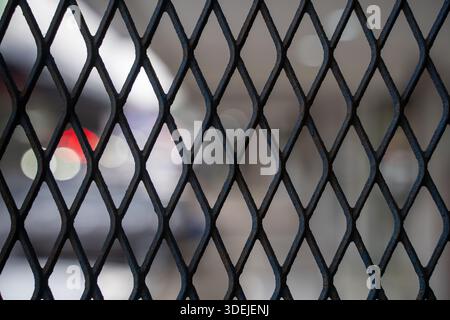 Close up of dark diamond pattern expanded metal mesh fence with blurred urban background bokeh Stock Photo