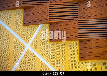 The tiered pattern of the wooden acoustic panels contrasts with the perforated yellow metal and crisscrossing white lines. Stock Photo