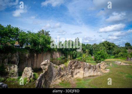 Scenic landscape of quarry cliffs, water, trees, and dramatic rock formations under a bright blue sky with white clouds, wide shot Stock Photo