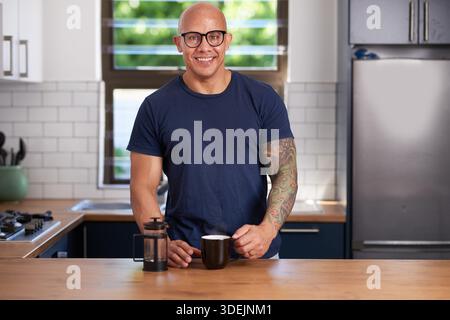 Confident Man With Tattooed Arm Enjoying Coffee In Modern Bright Kitchen At Home Stock Photo