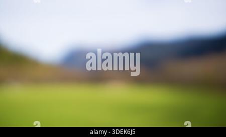 Soft focus creates smooth color transitions between grass, hills, and distant mountains. Stock Photo
