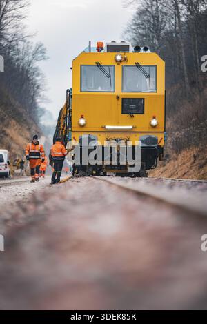 Close-up of a yellow train with workers on rails under cloudy sky, using a tamping machine on the Hermann Hessebahn construction site, Calw, Germany Stock Photo