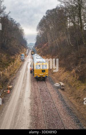 Train with construction workers on a rail line surrounded by winter forest, using a tamping machine at the Hermann Hessebahn construction site, Calw, Stock Photo