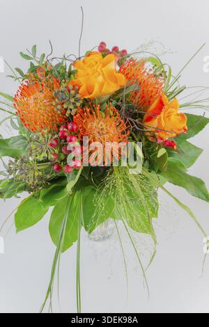 Colorful bouquet in a vase with orange and yellow flowers, red berries and green leaves, protea, roses Stock Photo