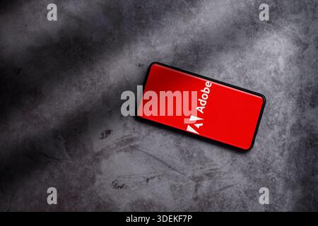 Flat lay photo of smartphone displaying Adobe logo on screen. Adobe creative computer software company. Stock Photo