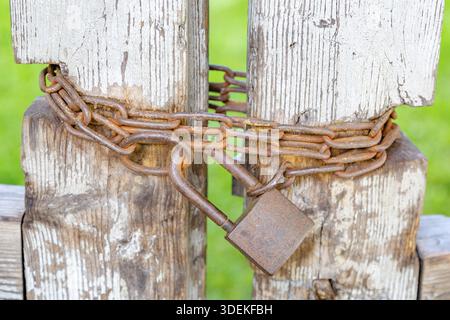 Old crooked gate closed on a large rusty padlock with chains Stock Photo