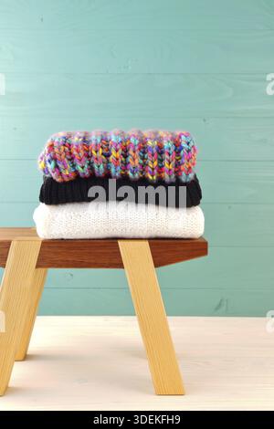 Stack of women's clothing. Warm female woollen knitted sweaters. winter and autumn fashion composition. pullovers stack on a wooden stool at wooden ba Stock Photo