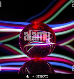 Glass ball on a black background with reflection in colored light rays, abstract Stock Photo