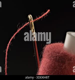 Red thread, threaded into a needle close-up on a black background Stock Photo