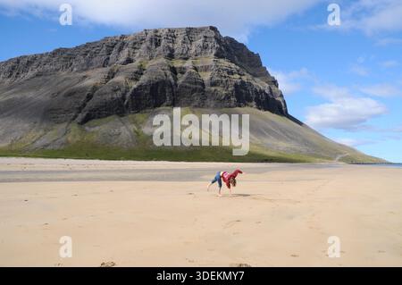 Young woman doing a cartwheel on a wide sandy beach in Iceland, expressing joy and freedom against a dramatic mountain landscape. Stock Photo