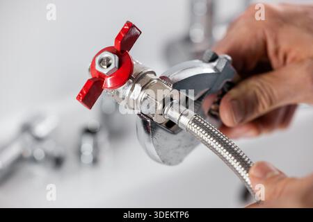 Plumber screws a flexible water pipe to a plumbing valve Stock Photo