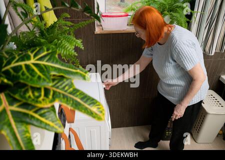 Overhead view of a senior woman's hands pressing buttons on the control panel of a modern washing machine to start a laundry cycle. Stock Photo