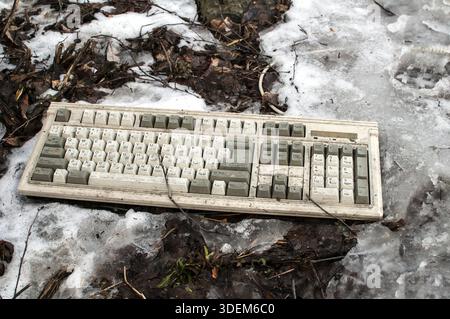 Abandoned dirty broken grunge computer keyboard on snowy frozen soil Stock Photo