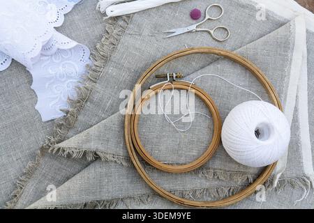 Set for embroidery, garment needle, thread, scissors and embroidery hoop on unbleached linen fabric. Top view Stock Photo