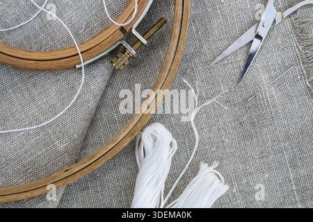 Set for embroidery, garment needle, thread, scissors and embroidery hoop on unbleached linen fabric. Top view Stock Photo