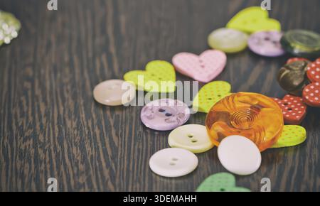 Buttons of different shapes and colors lying on a dark wooden table Stock Photo