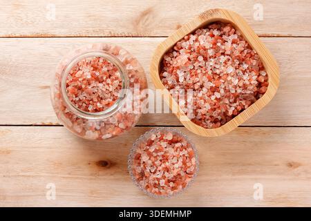 Himalayan salt crystals in wooden and glass containers on a light wood table. Top view. Stock Photo