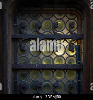 Close-up of an antique church window with circular glass panes and wrought iron bars, illuminated from inside. Historic stained glass window detail. Stock Photo