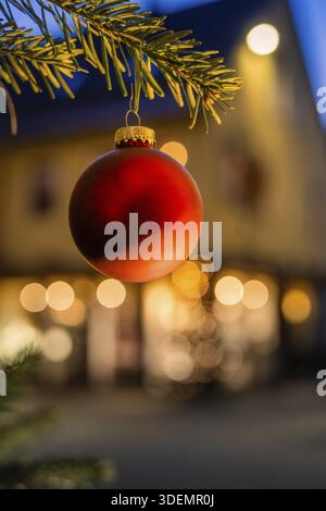 Red Christmas ball on pine branch, blurred background with lights, Nagold, Calw district, Black Forest, Germany Stock Photo