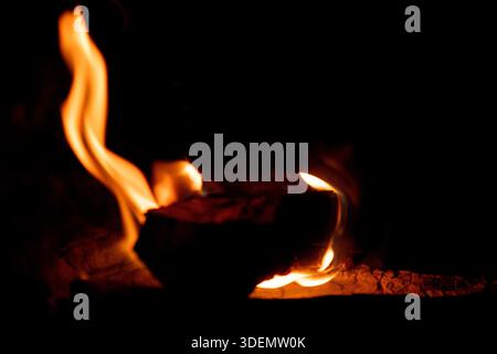 Close-up of bright orange and yellow fire flames burning logs against a stark black background. Stock Photo