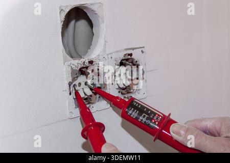 Hand of Electrician testing for electricity with a voltage tester. Electrician checking wall socket with voltage tester. Touchless Voltage tester hand Stock Photo